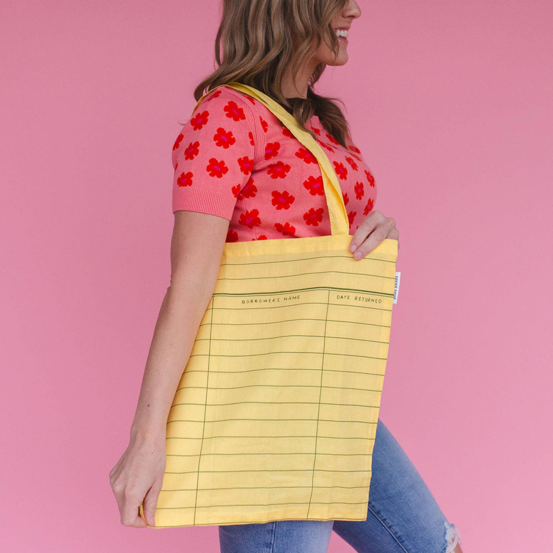 Woman holding a yellow tote bag with a pink background