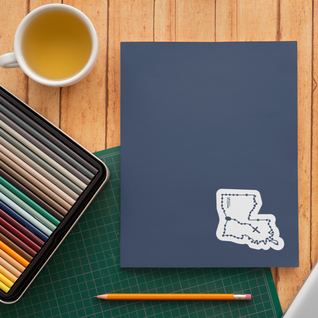 Blue notebook with a white outline of a state on a wooden table with a cup of tea, colored pencils, and a pencil.