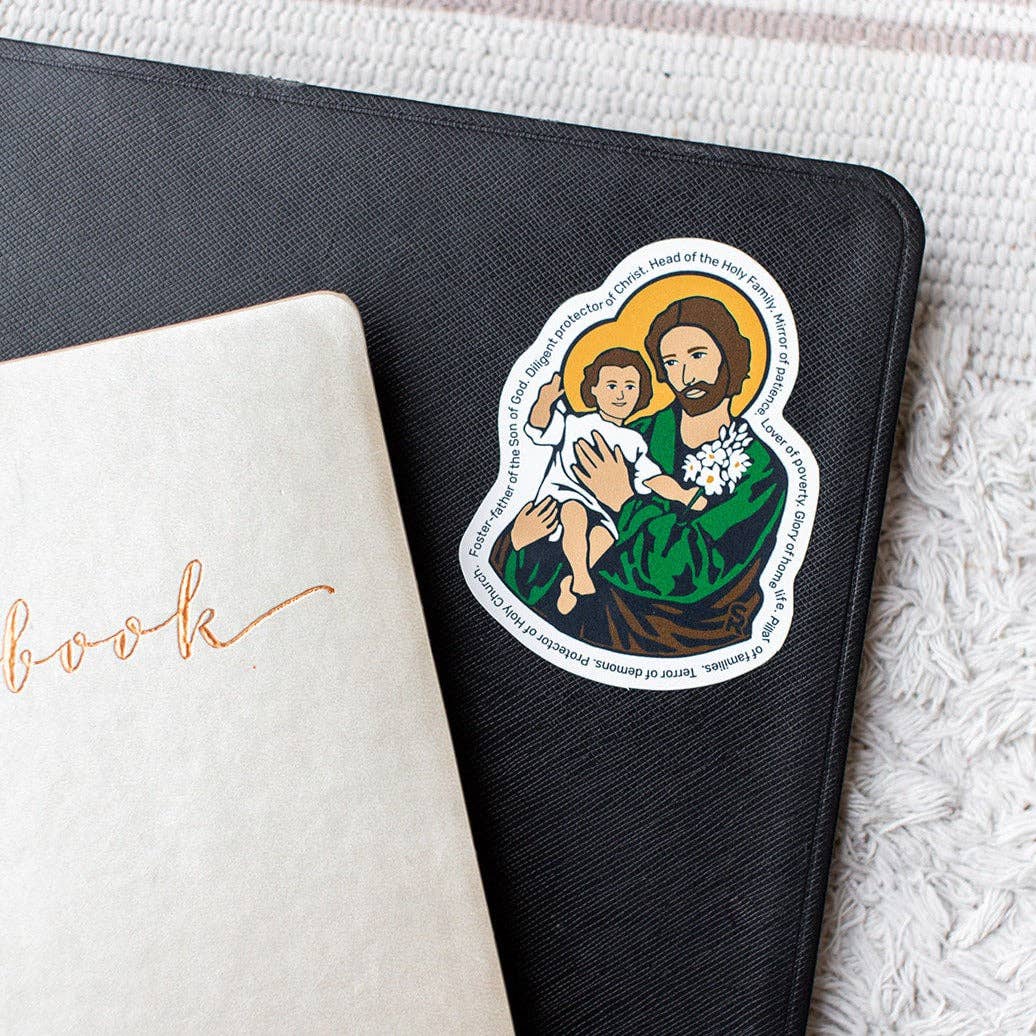 Sticker of a religious figure holding a child on a black notebook with a white book underneath.
