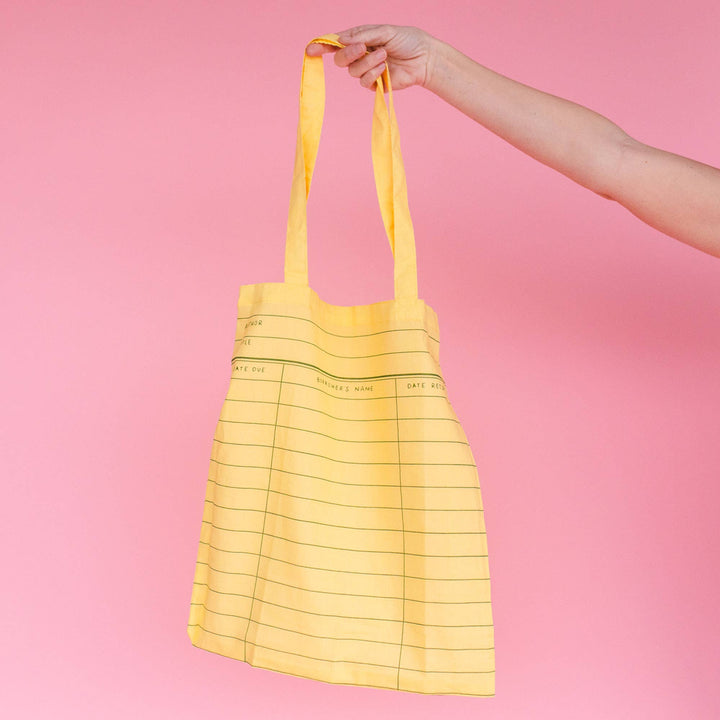 Yellow tote bag with grid pattern held against a pink background