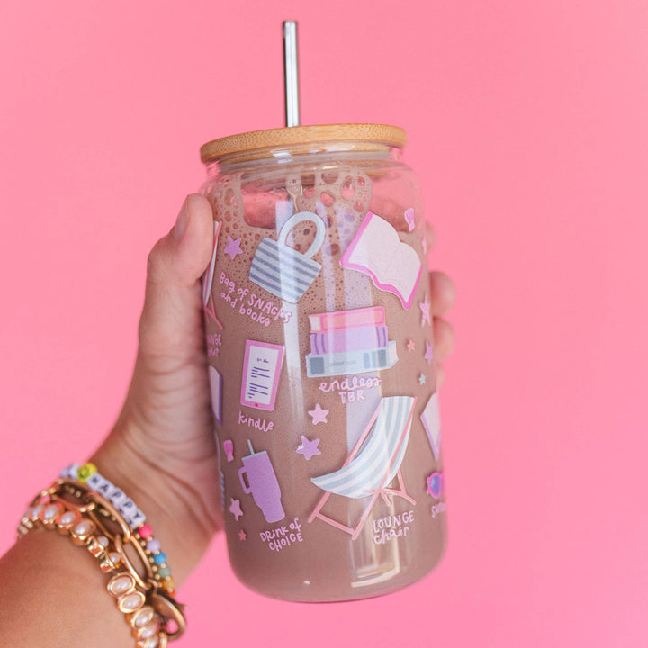 Glass tumbler with a straw and decorative stickers held by a hand against a pink background