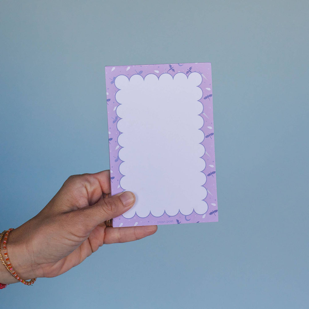 Hand holding a purple notepad with white scalloped border against a blue background