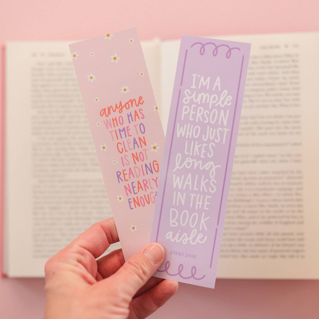 Two bookmarks with humorous text held over an open book on a pink background