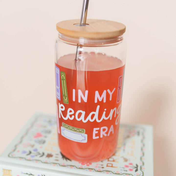 Clear tumbler with wooden lid and straw, filled with red liquid, on a floral coaster.