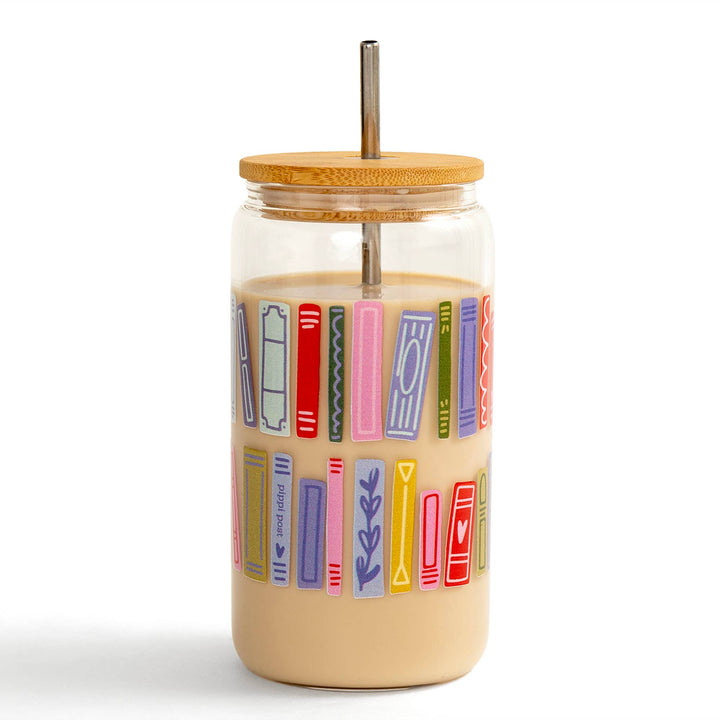 Glass tumbler with colorful book illustrations, wooden lid, and metal straw on a white background