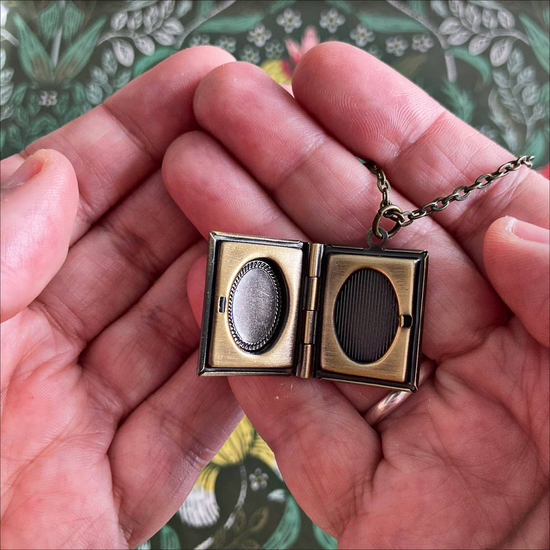 Small brass locket held in hands with a floral patterned background