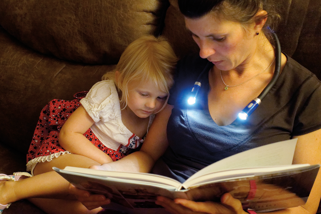 Woman and child reading a book with neck lights on a couch