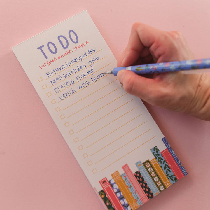 Hand writing on a to-do list with a pen against a pink background