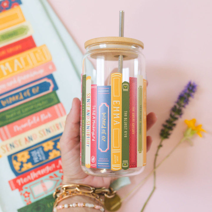 Hand holding a clear jar with colorful book-shaped objects and a straw, against a light background.