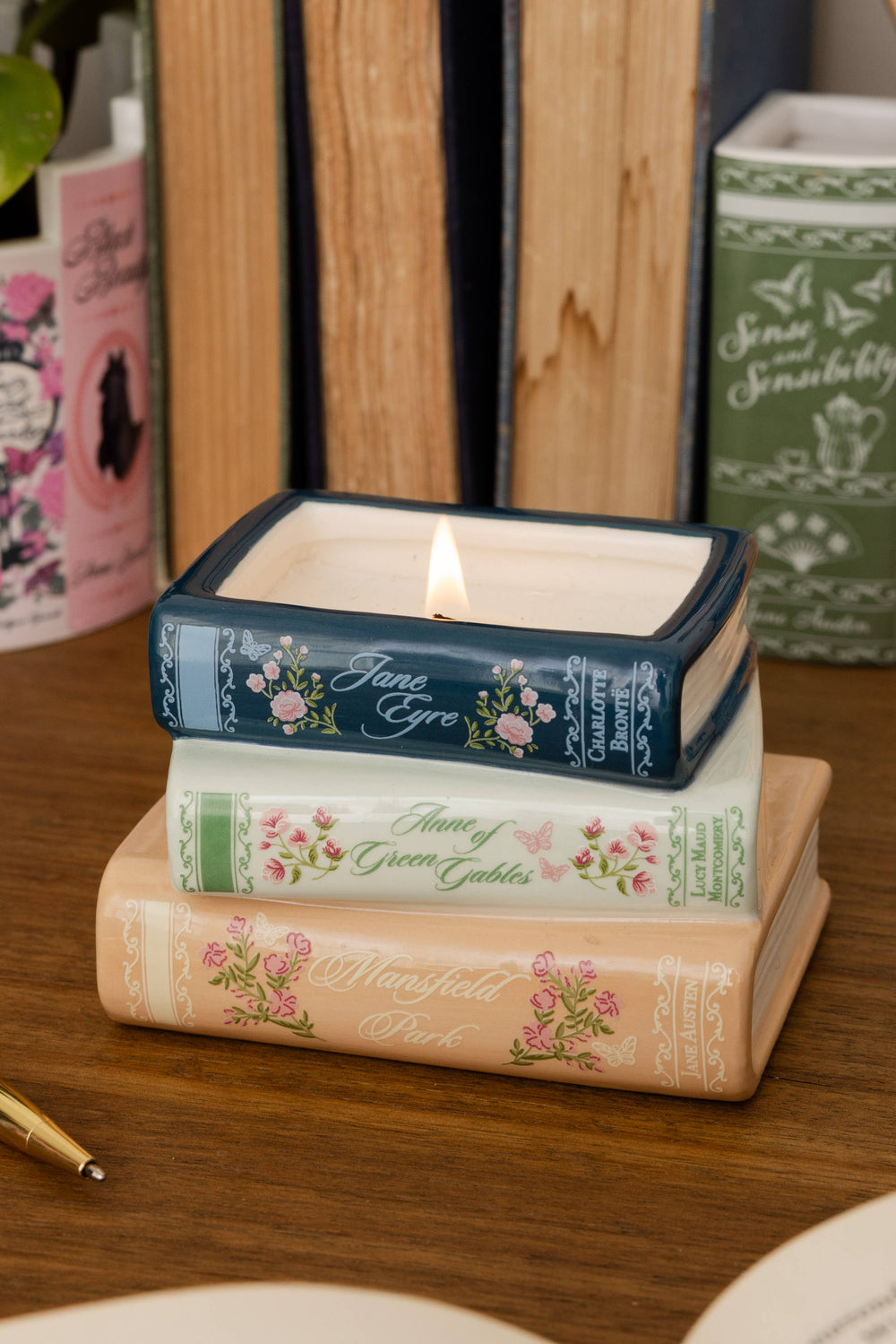 A square candle in a dark blue tin with floral detailing and the name 'Jane Eyre' on the lid, styled on top of two decorative book spines on a wooden table.