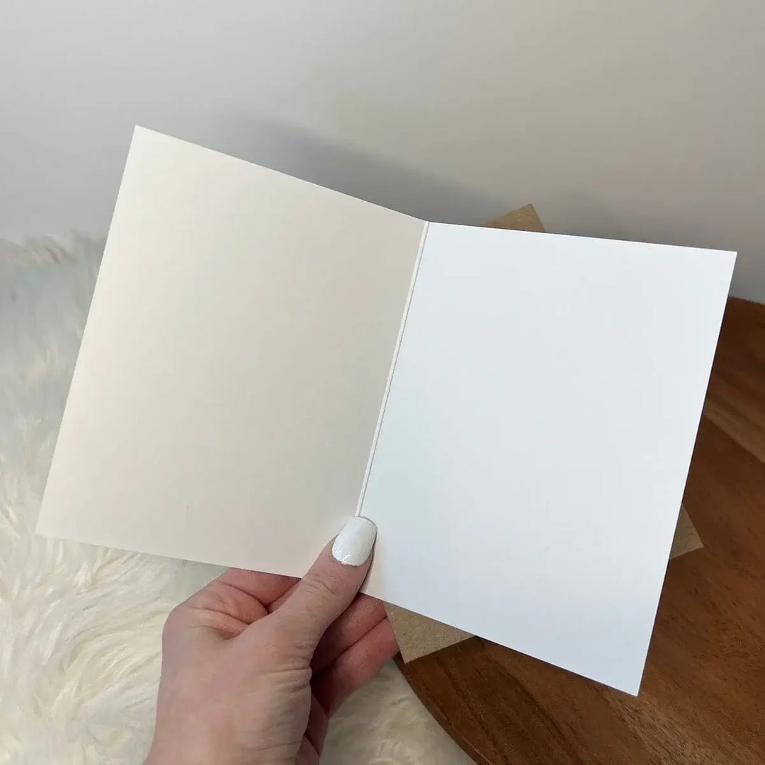 Hand holding an open white card against a neutral background