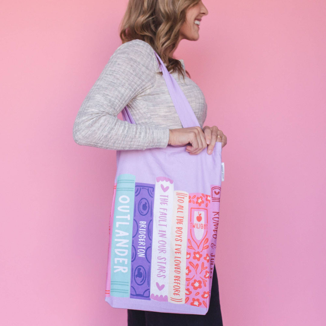 Woman holding a tote bag with book design against a pink background