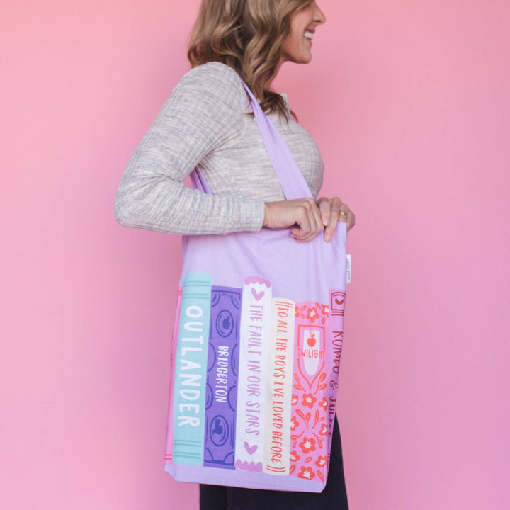 Woman holding a tote bag with book design against a pink background