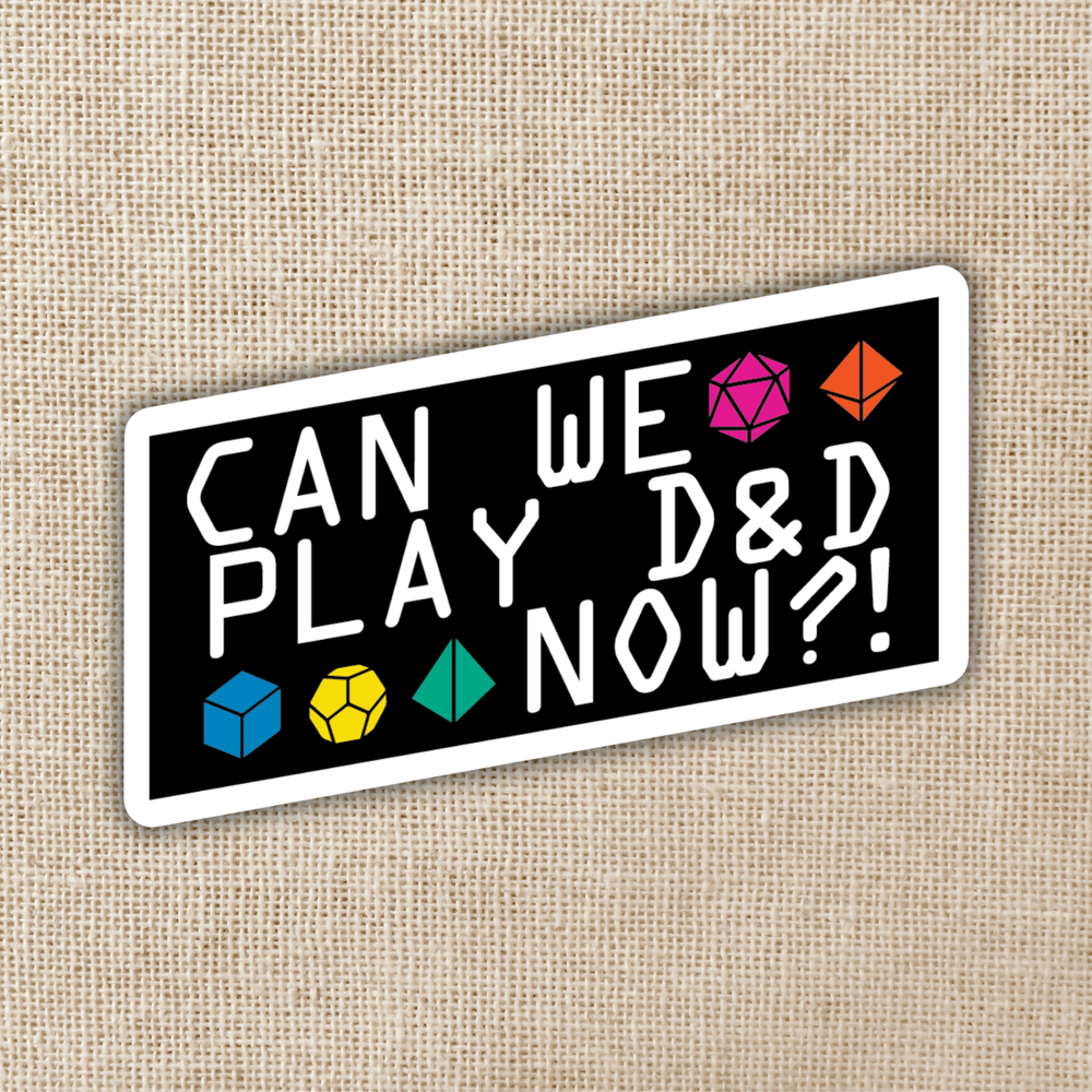 Sticker with text 'Can we play D&D now?' and gaming dice symbols on a beige fabric background