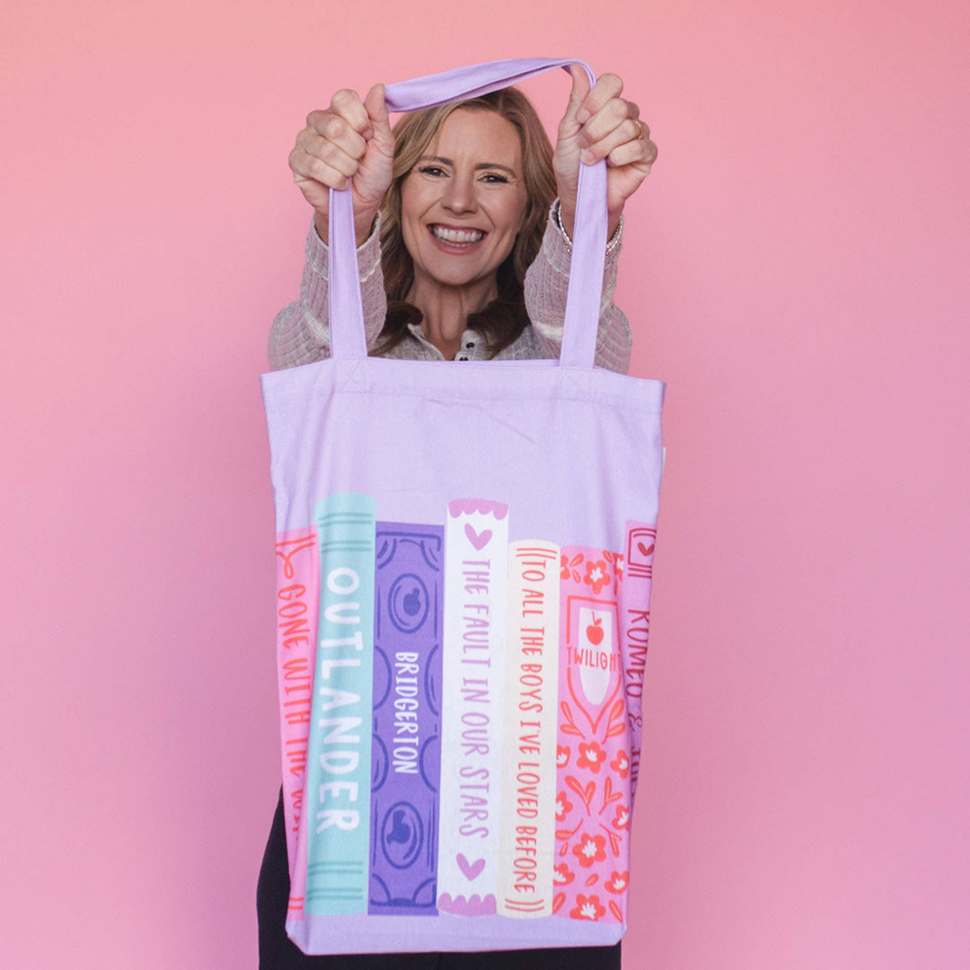 Woman holding a tote bag with book-themed design against a pink background