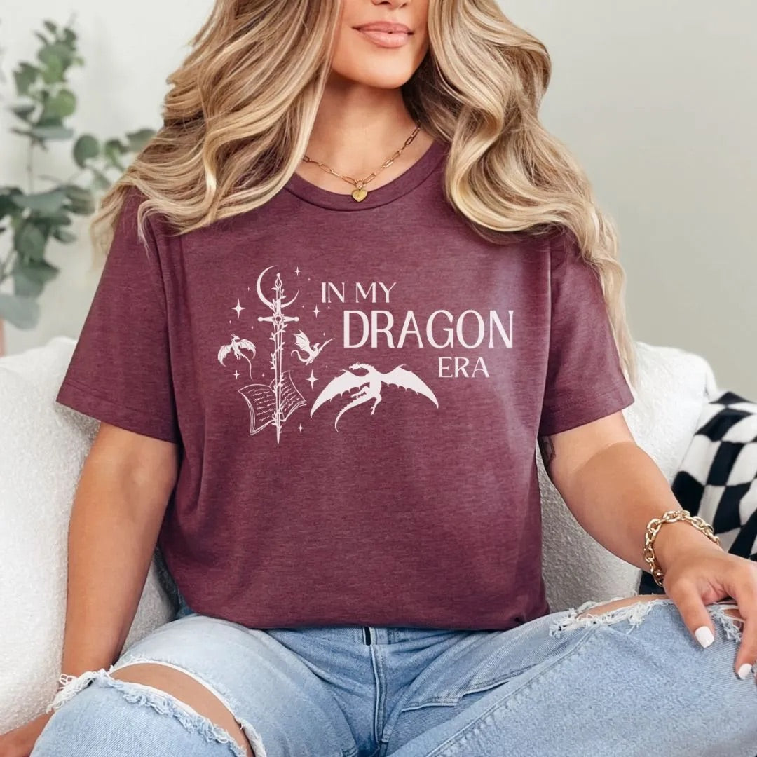 Person wearing a maroon t-shirt with 'In My Dragon Era' text and graphics.