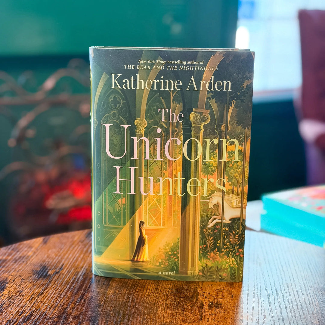Book titled 'The Unicorn Hunters' by Katherine Arden on a wooden table with a blurred background