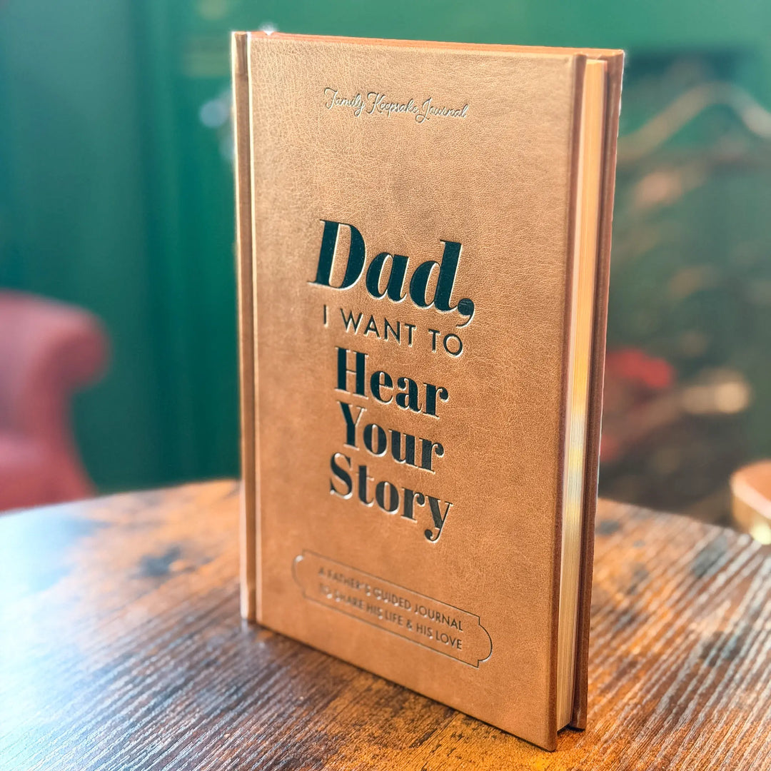 Brown journal titled 'Dad, I Want to Hear Your Story' on a wooden surface with a blurred background