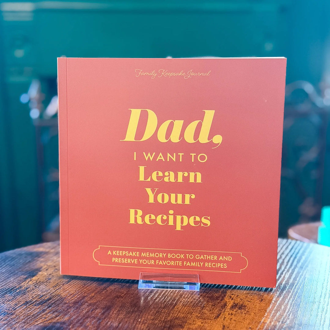 Book titled 'Dad, I Want to Learn Your Recipes' on a wooden surface with a blurred background