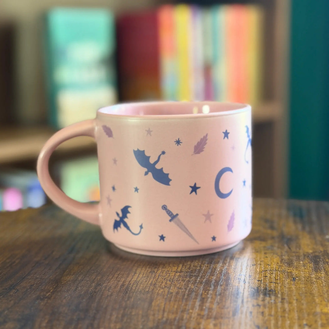 Pink mug with fairy designs on a wooden table with colorful books in the background