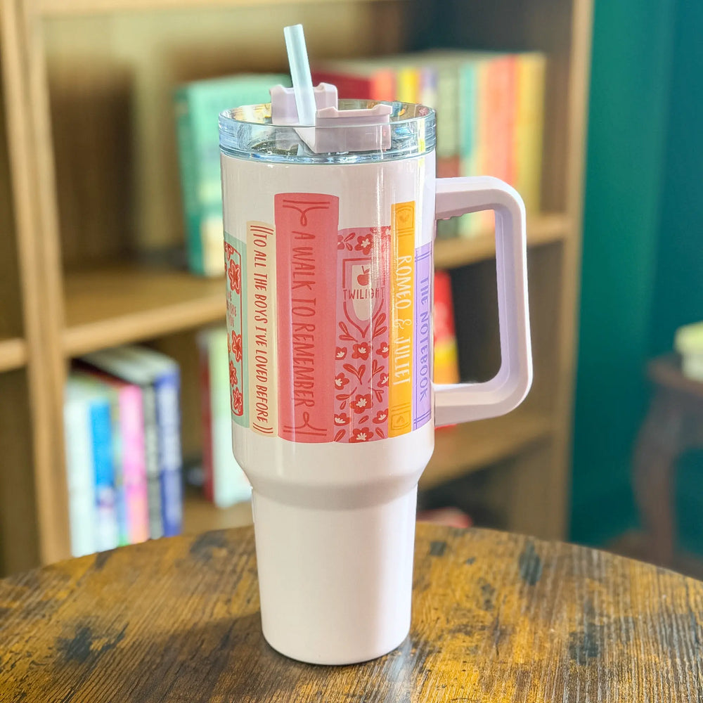 White tumbler with colorful design on a wooden table with a bookshelf in the background