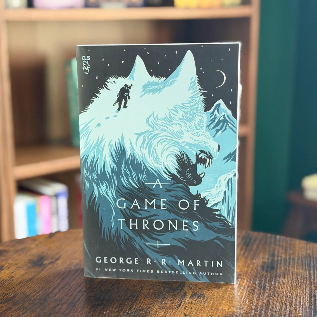 Book titled 'A Game of Thrones' by George R.R. Martin on a wooden surface with a blurred bookshelf background.