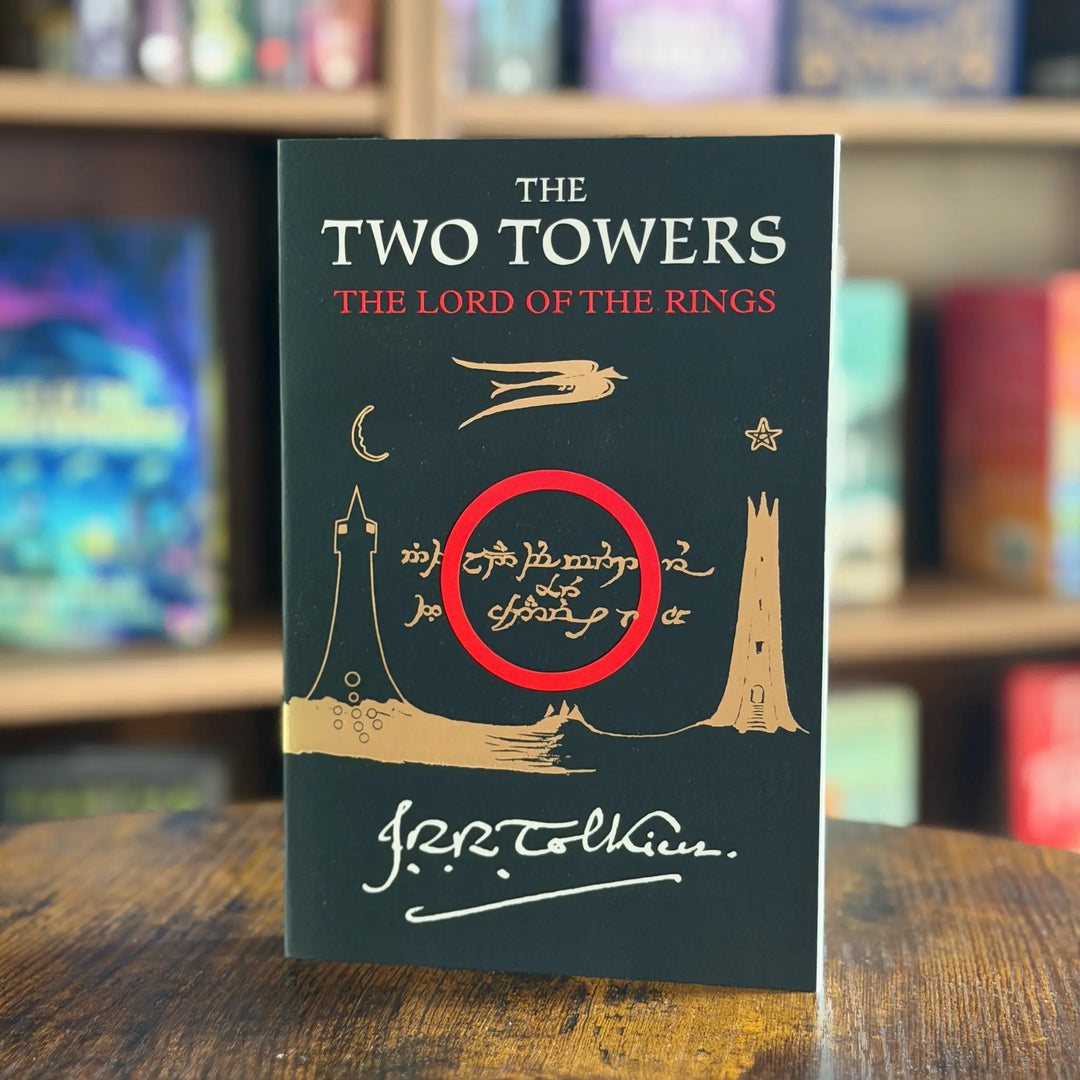 The Two Towers book on a wood table with a blurred bookshelf background