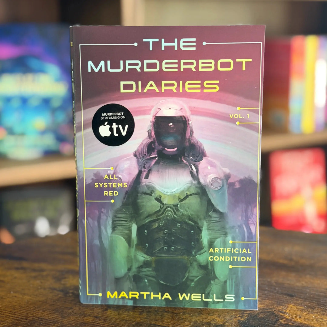 Book titled 'The Murderbot Diaries' by Martha Wells on a wooden surface with a blurred colorful background.