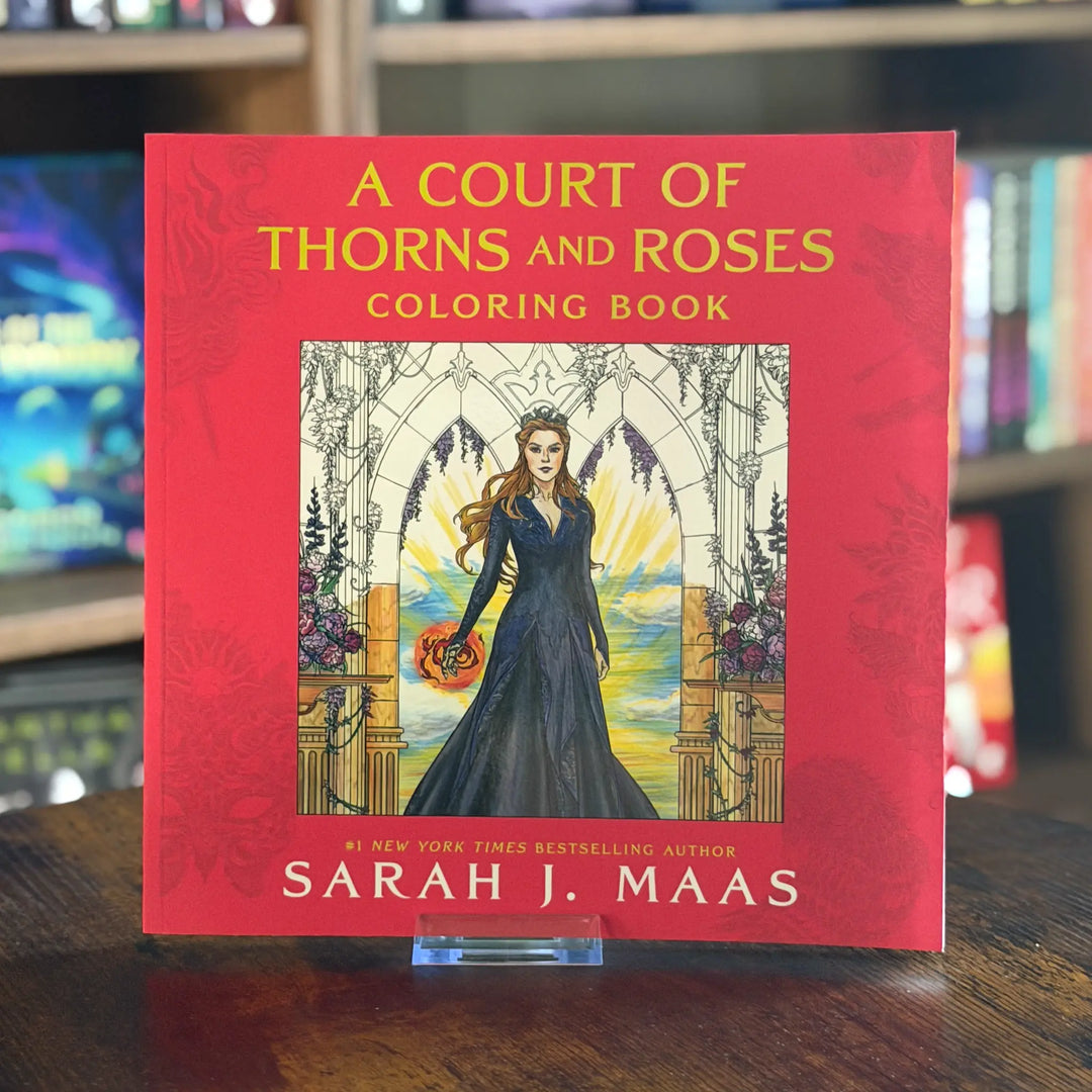 Coloring book titled 'A Court of Thorns and Roses' by Sarah J. Maas on a wooden surface with a blurred bookshelf background.