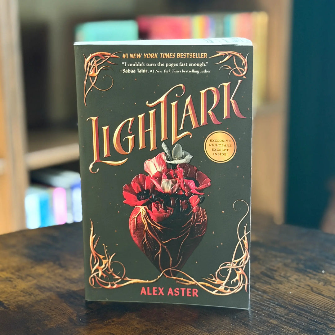 Book titled 'Lightlark' by Alex Aster on a wooden surface with blurred books in the background