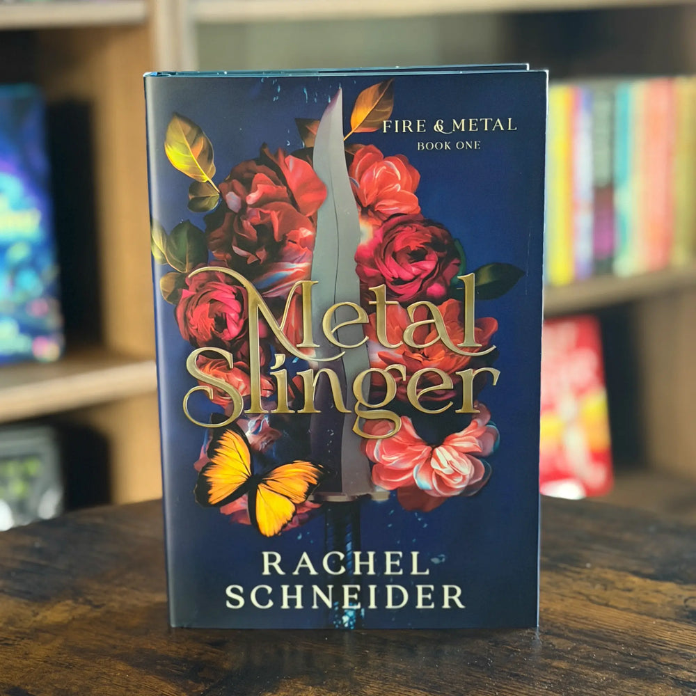 Book titled 'Metal Slinger' by Rachel Schneider on a wooden surface with a blurred bookshelf background.
