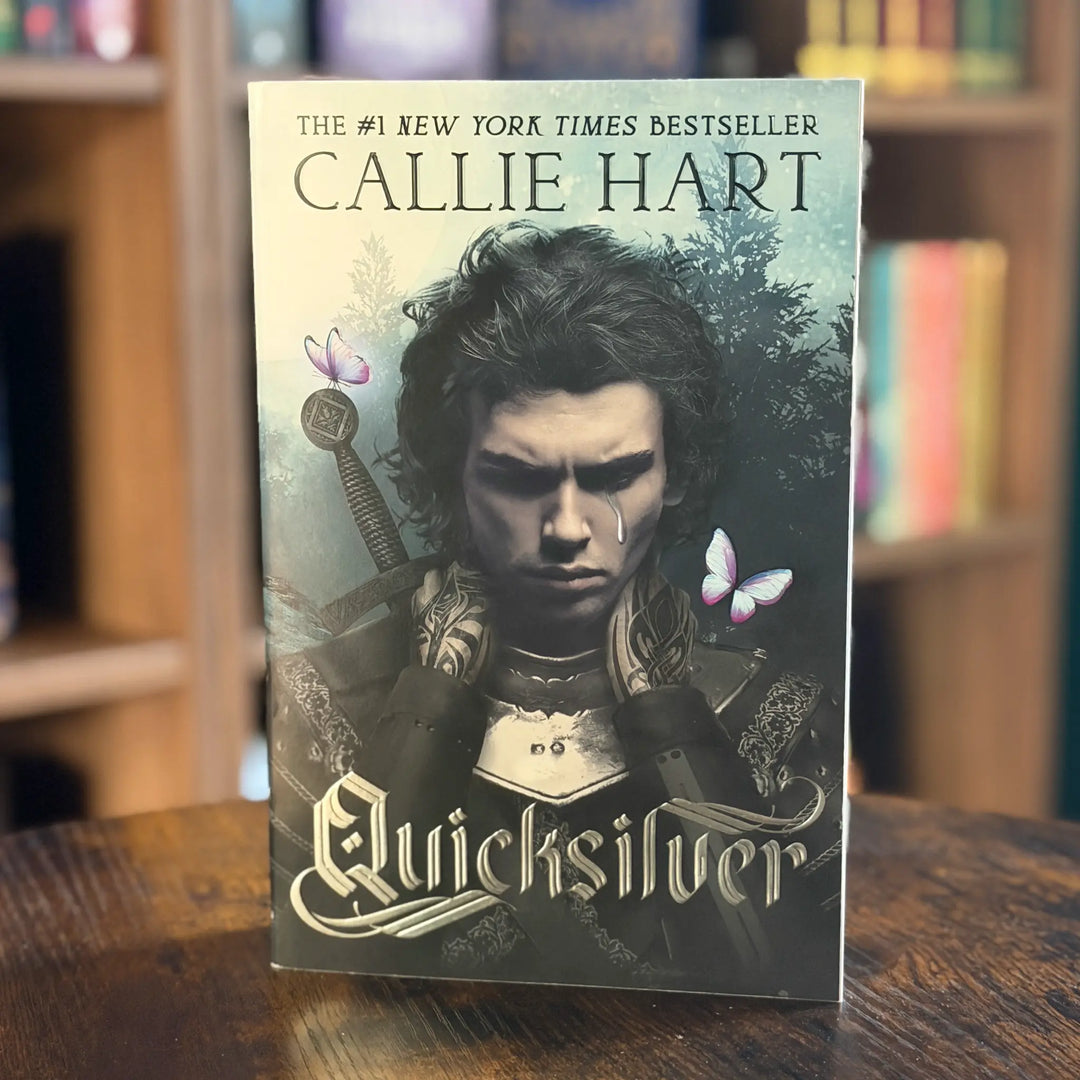 Book titled 'Quicksilver' by Callie Hart on a wooden surface with a blurred bookshelf background.