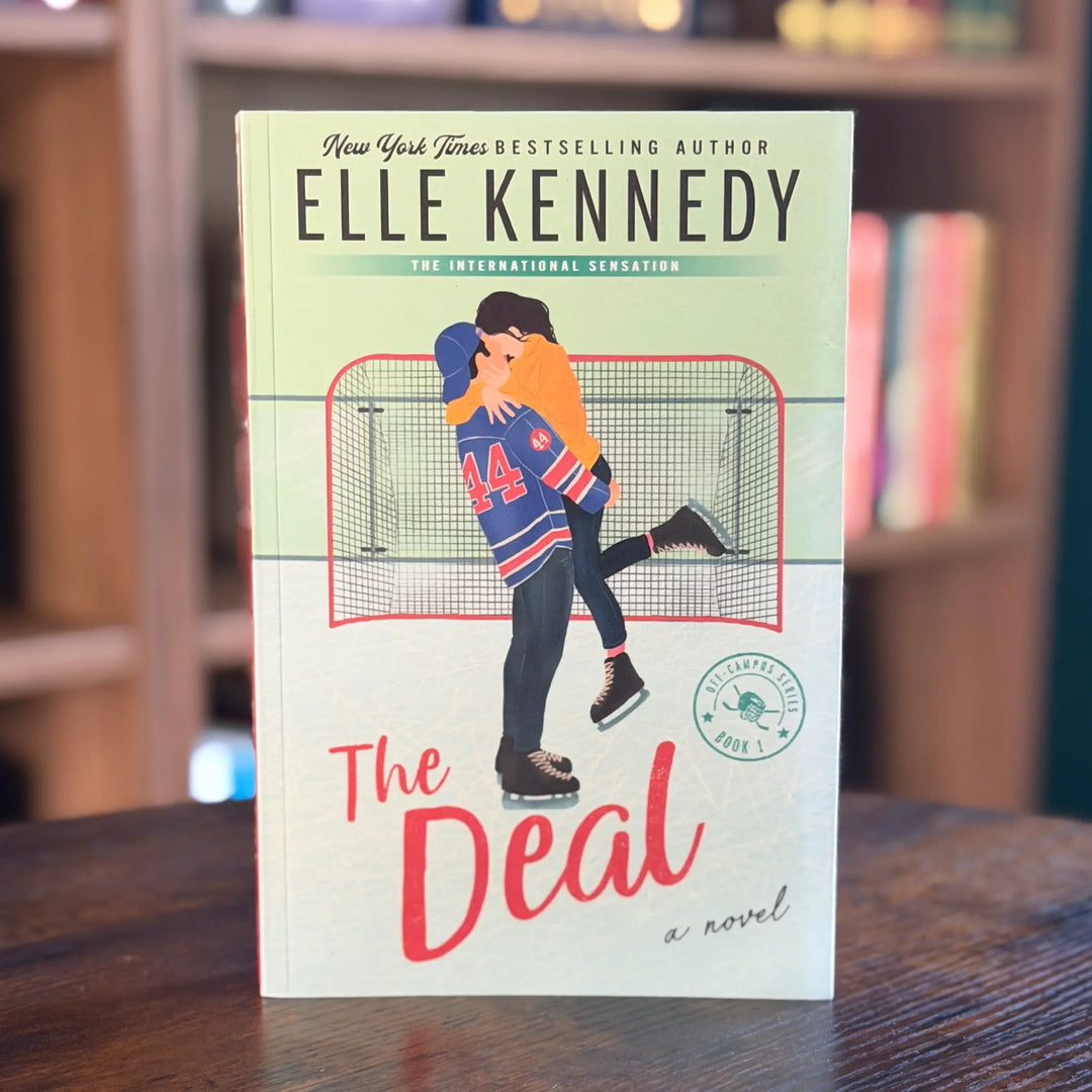 Book titled 'The Deal' by Elle Kennedy on a wooden surface with a blurred bookshelf background