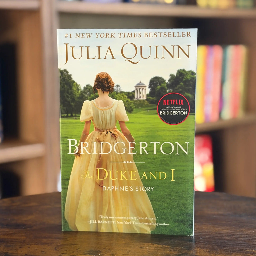 Book titled 'Bridgerton: The Duke and I' by Julia Quinn on a wooden surface with a blurred bookshelf background.
