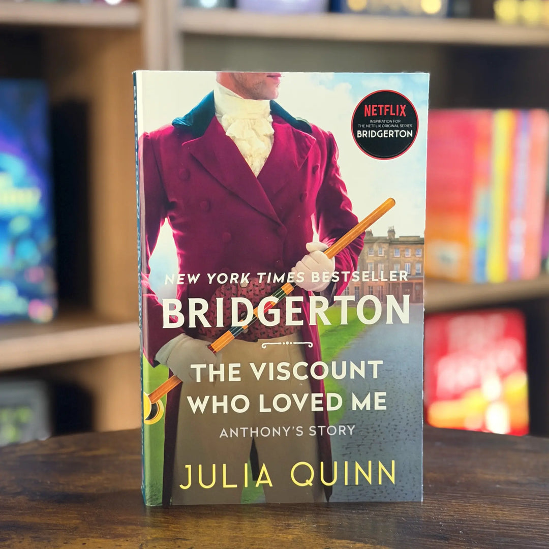 Book titled 'Bridgerton: The Viscount Who Loved Me' by Julia Quinn on a wooden surface with a blurred bookshelf background.