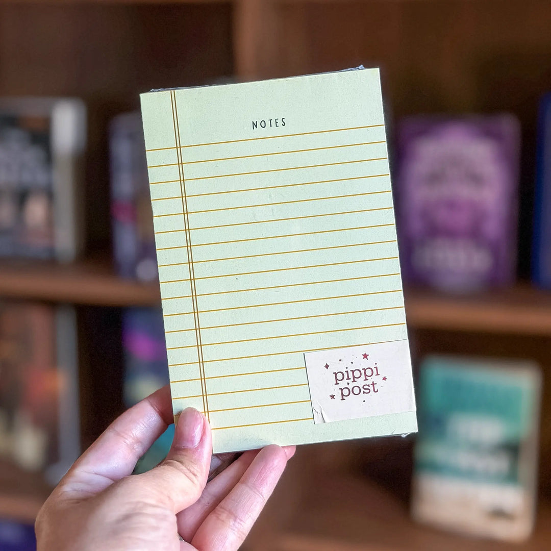 Hand holding a notepad with 'pippi post' branding against a blurred bookshelf background