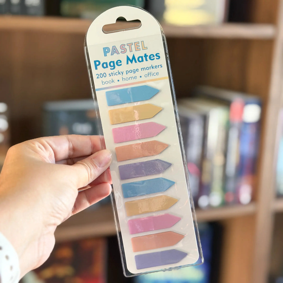 Pack of Pastel Page Mates sticky page markers held by a hand with a blurred bookshelf background.
