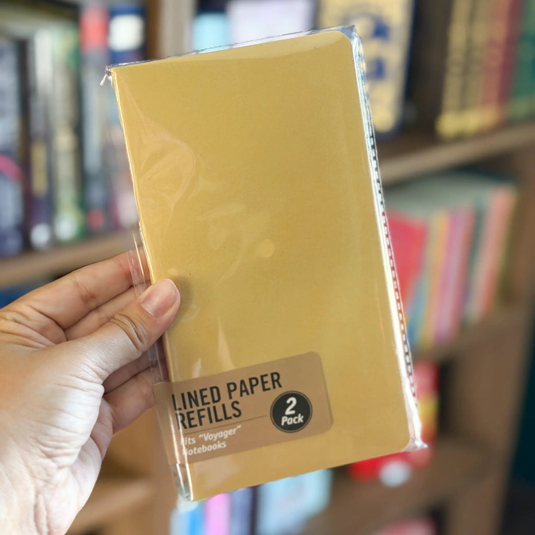 Hand holding a package of lined paper refills in front of a bookshelf.