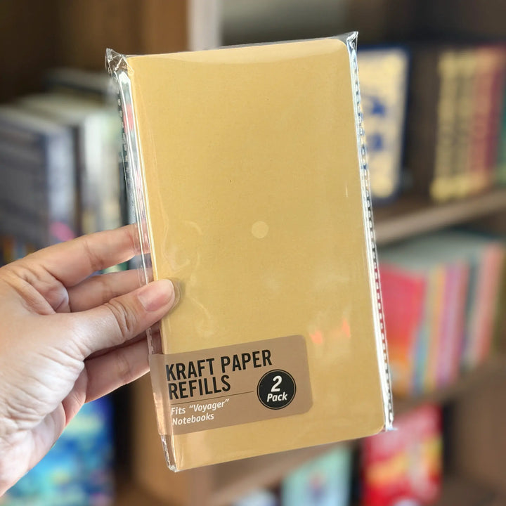 Hand holding a package of Kraft Paper Refills with a blurred bookshelf background