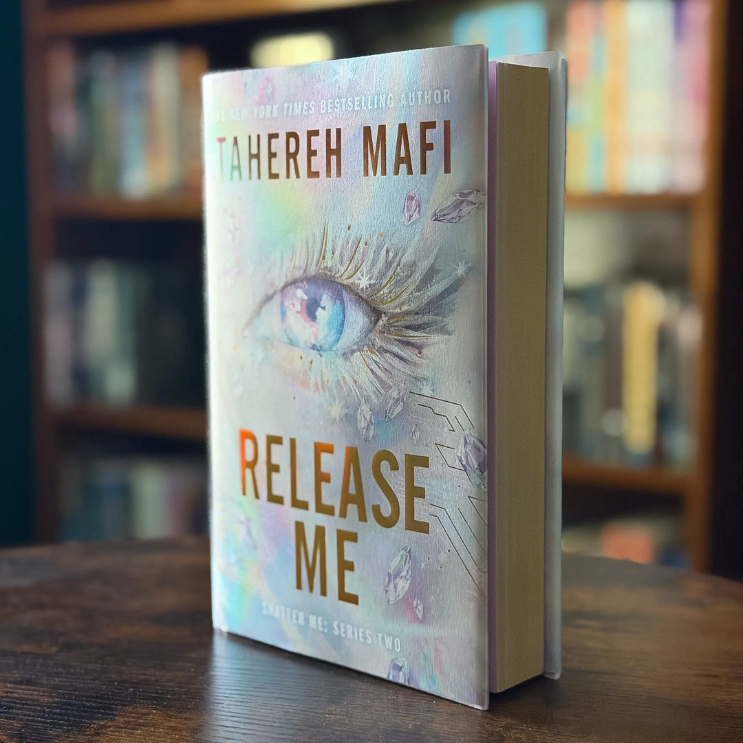 Book titled 'Release Me' by Tahereh Mafi on a wooden surface with a blurred bookshelf background
