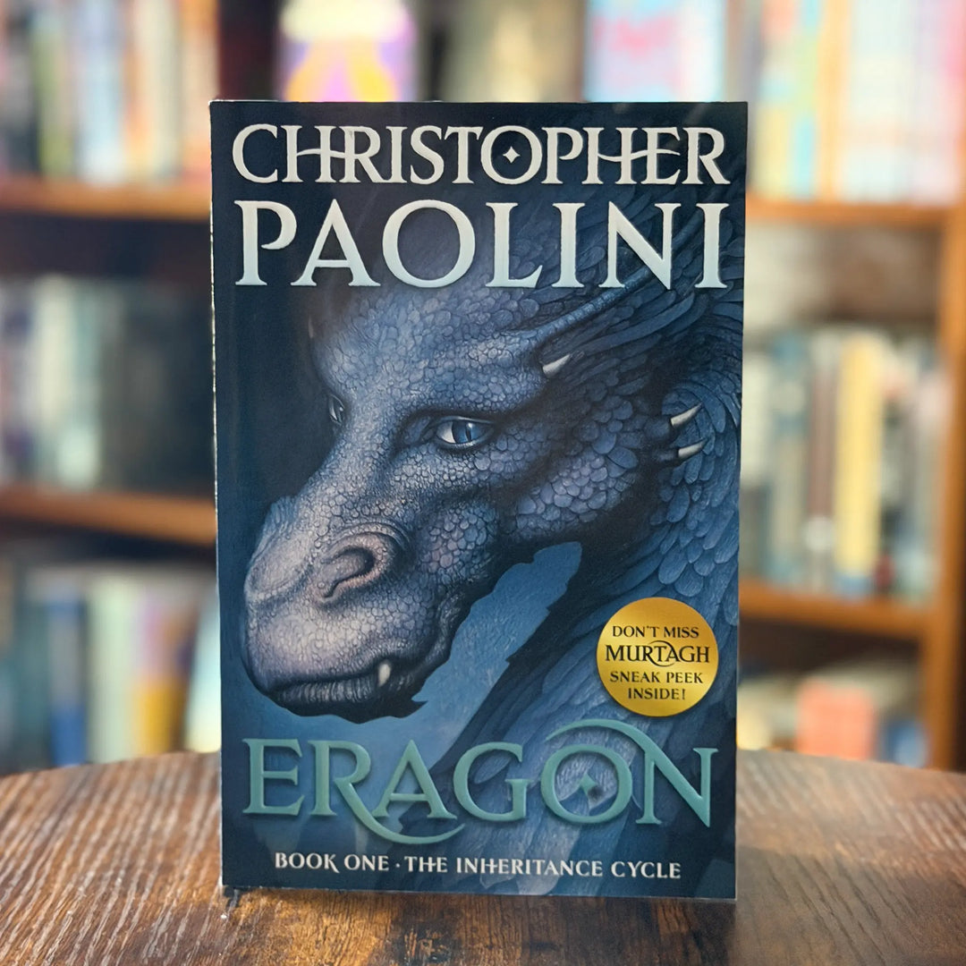 Book cover of 'Eragon' by Christopher Paolini with a dragon illustration on a wooden surface.