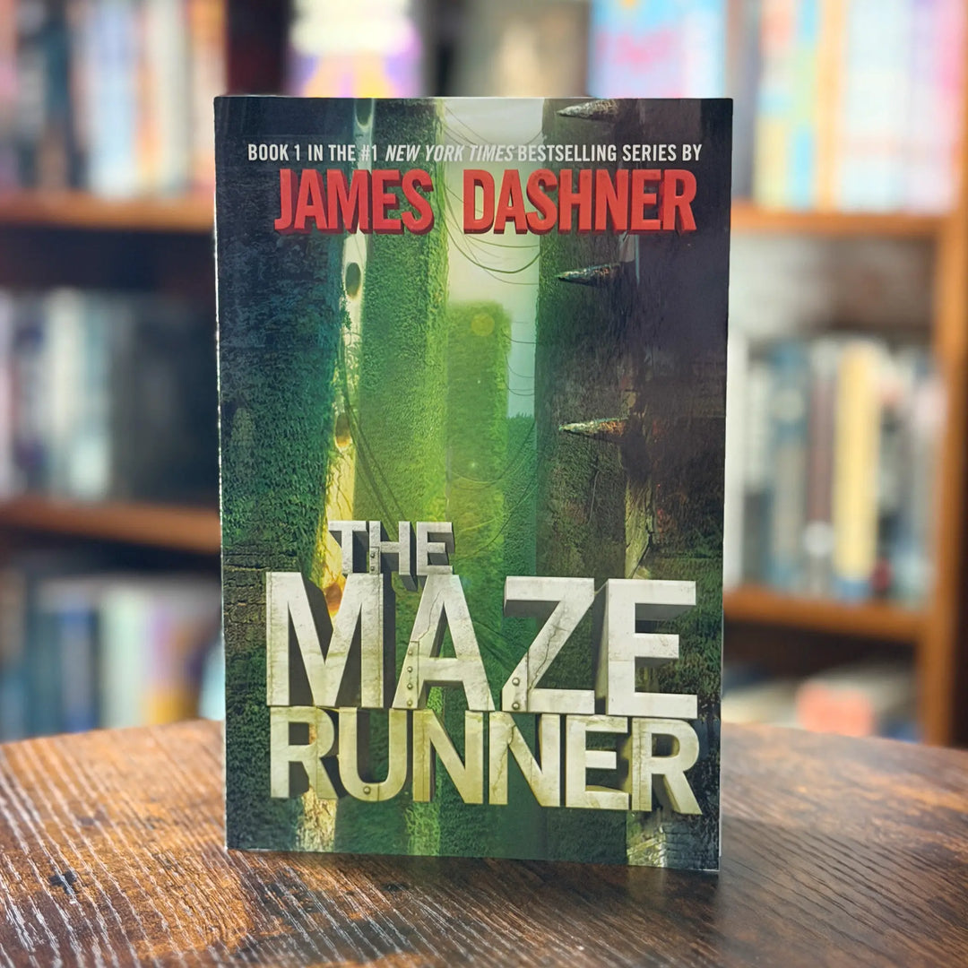 Book titled 'The Maze Runner' by James Dashner on a wooden surface with a blurred bookshelf background.