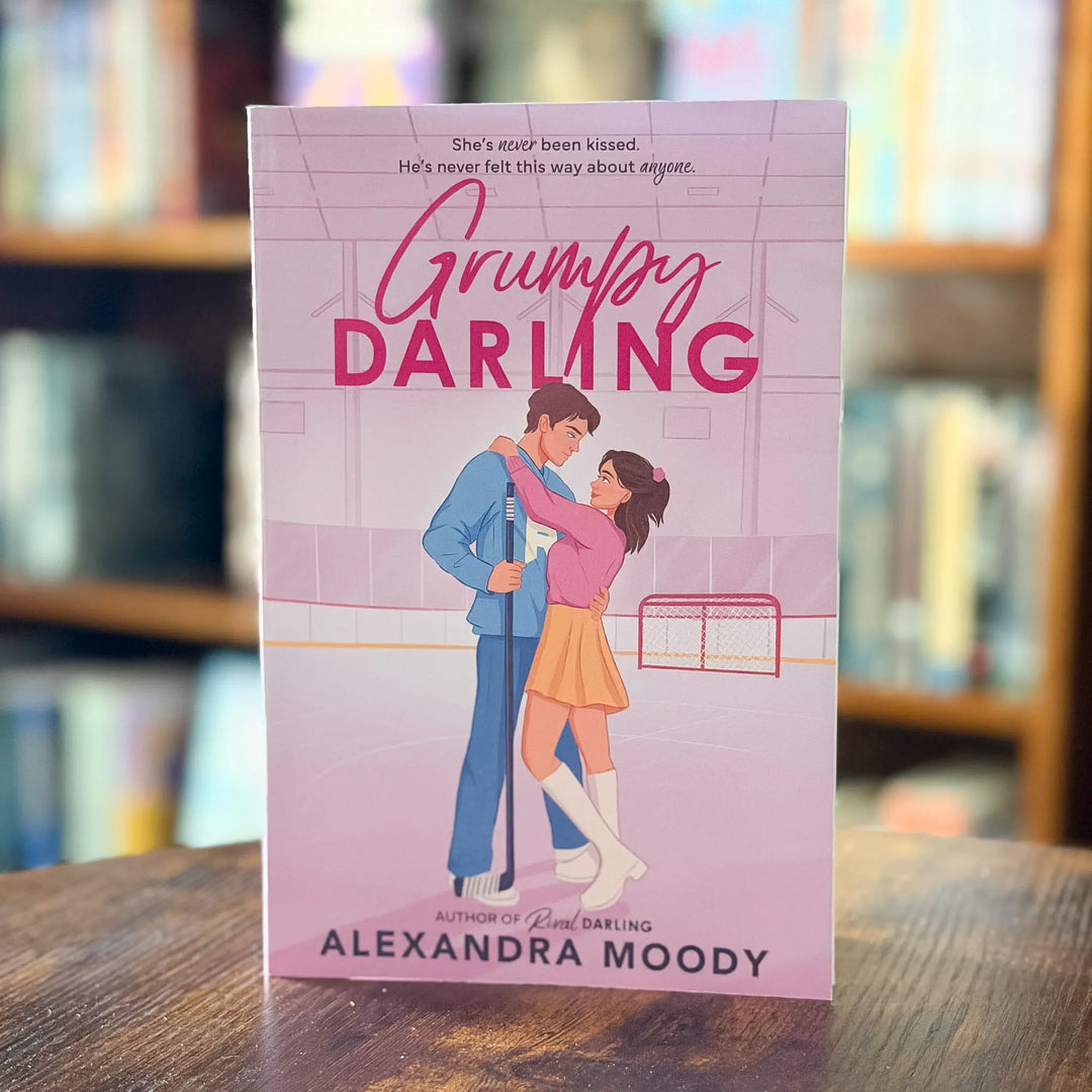 Book cover of 'Grumpy Darling' by Alexandra Moody on a wooden surface with a blurred bookshelf background.