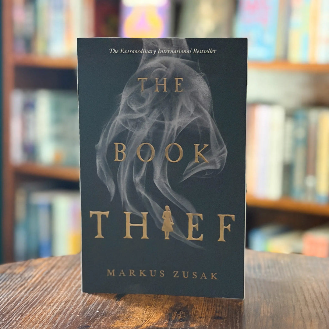 Book titled 'The Book Thief' by Markus Zusak on a wooden surface with a blurred bookshelf background.