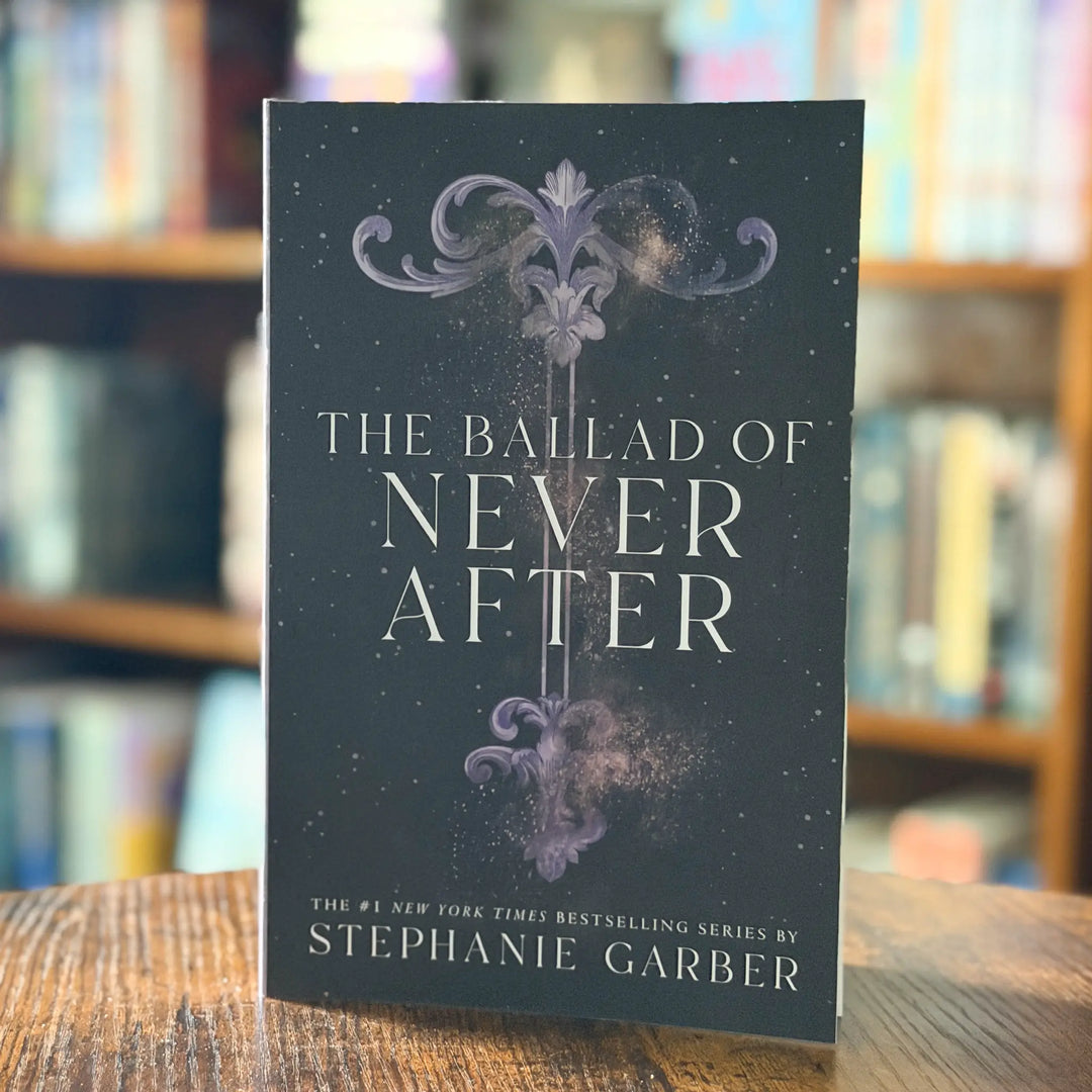 Book titled 'The Ballad of Never After' by Stephanie Garber on a wooden surface with a blurred bookshelf background.