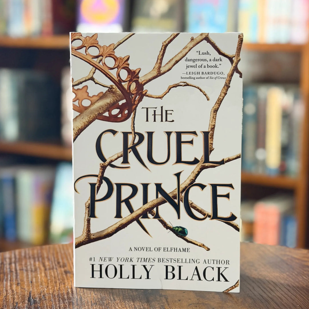 Book titled 'The Cruel Prince' by Holly Black on a wooden surface with a blurred bookshelf background.