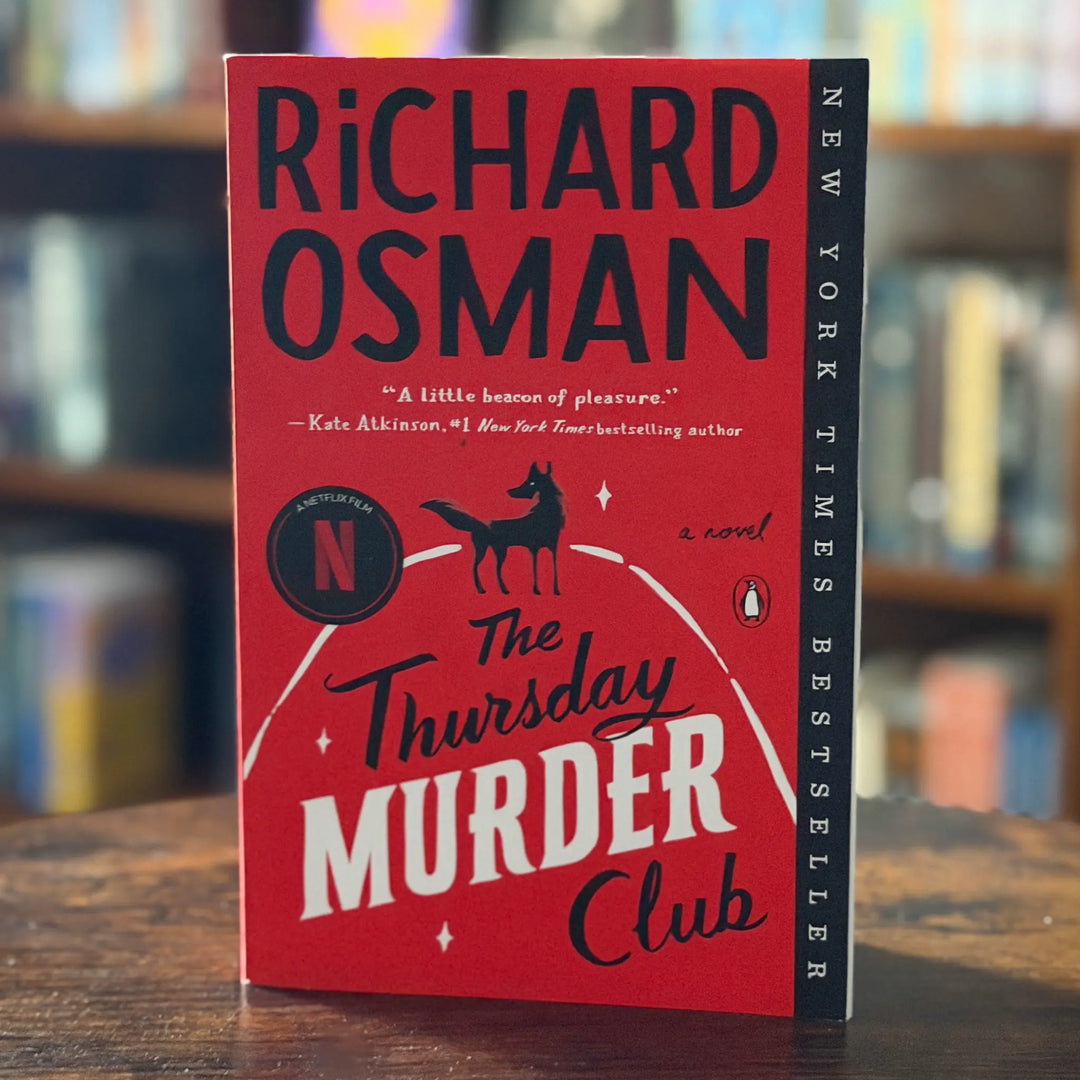 Book titled 'The Thursday Murder Club' by Richard Osman on a wooden surface with a blurred bookshelf background.