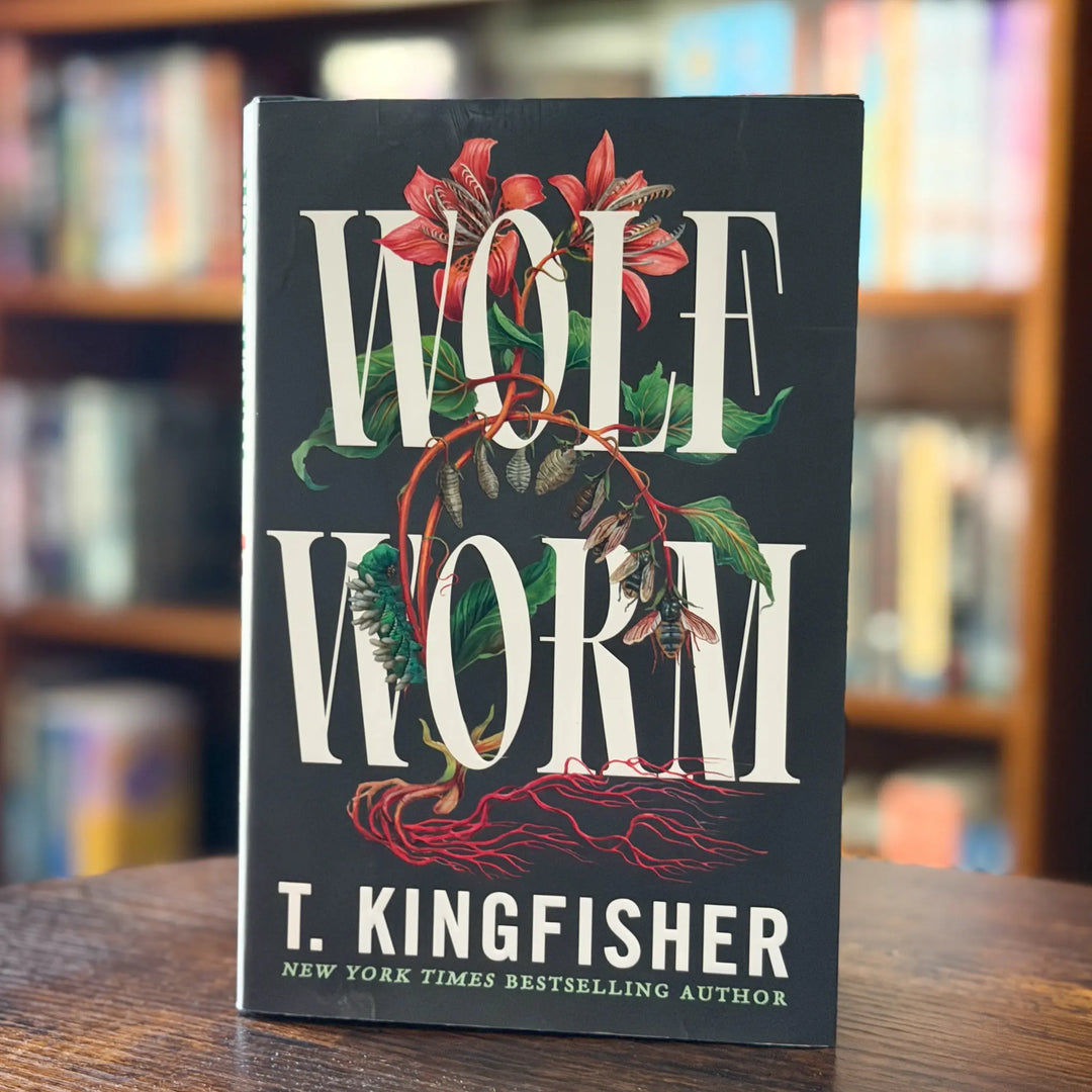 Book titled 'Wolf Worm' by T. Kingfisher on a wooden surface with a blurred bookshelf background.