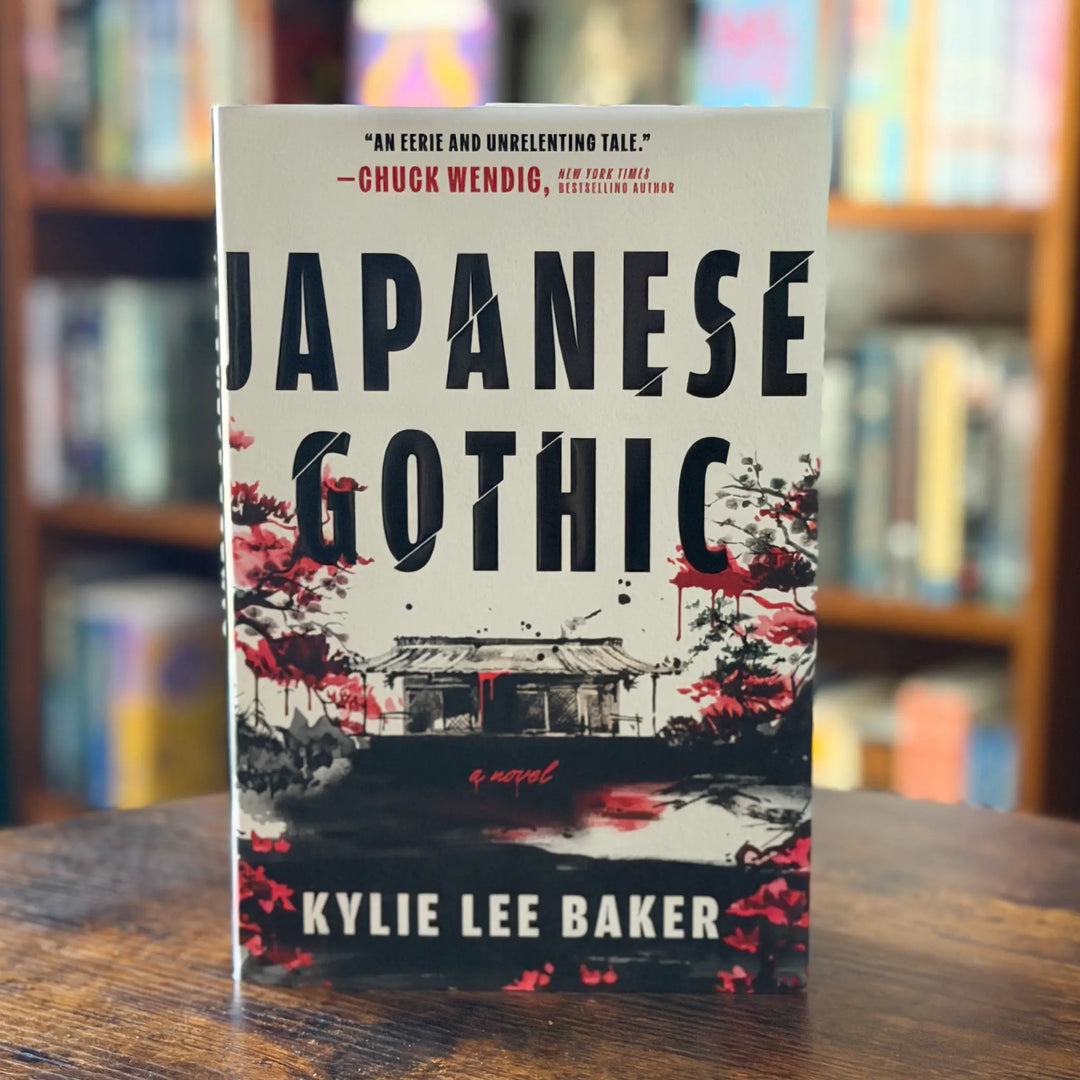 Book titled 'Japanese Gothic' by Kylie Lee Baker on a wooden surface with a blurred bookshelf background.