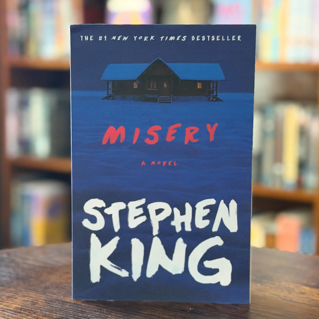 Book cover of 'Misery' by Stephen King with a blurred bookshelf background